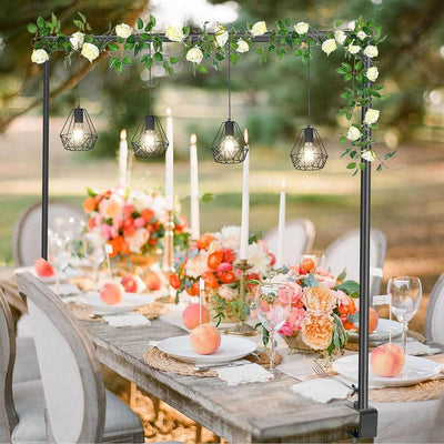 Decorative outdoor table setting with floral arch, candles, and fruit.