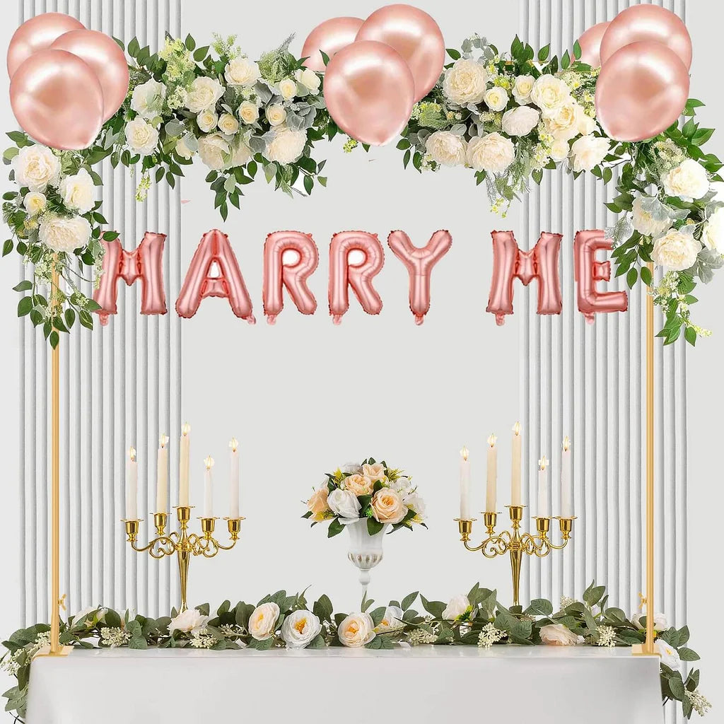 Decorated table with 'MARRY ME' balloons, flowers, and candles on a white background