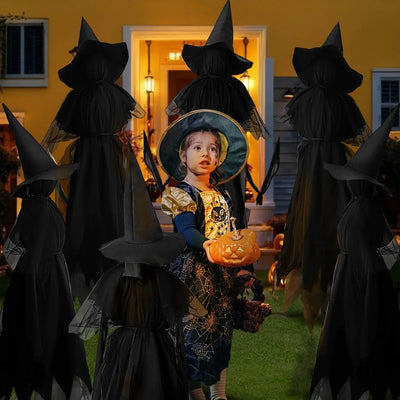 Child in a witch costume with a pumpkin, surrounded by other witch figures in front of a house.