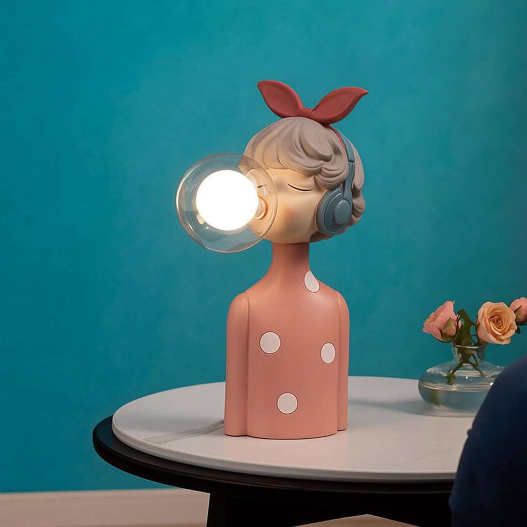 Decorative lamp shaped like a girl with a bow on her head, wearing headphones, on a table against a blue background.