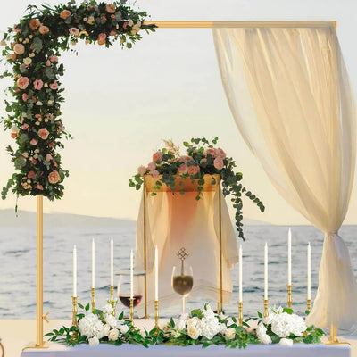 Decorative setup with floral arch, candles, and tablecloth by a body of water.