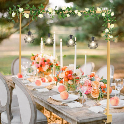Decorated outdoor table with floral arrangements, candles, and hanging lights.