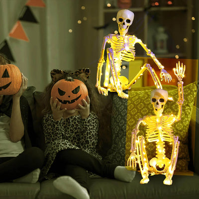 Children with pumpkin masks and a lit-up skeleton on a couch in a Halloween-themed room.