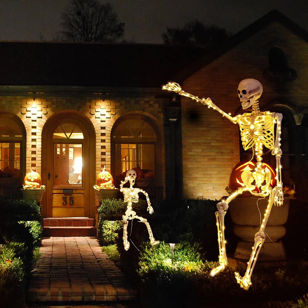 Halloween decorations including skeletons and a pumpkin with lights in front of a house.