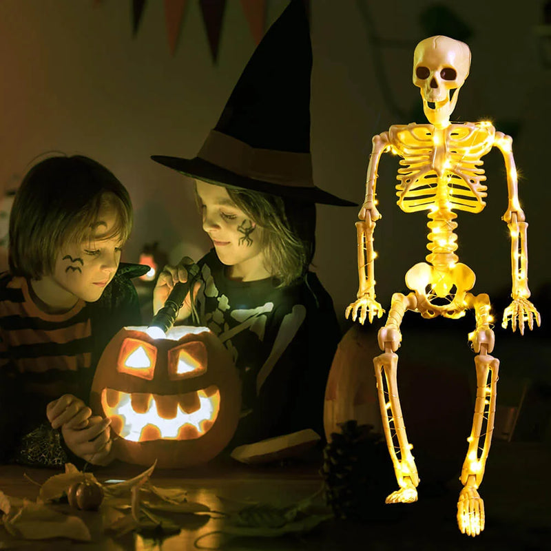 Two children in Halloween costumes with a lit jack-o'-lantern and a skeleton figure.
